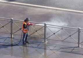 Worker cleaning driveway with gasoline high pressure washer splashing the dirt, asphalt road fence. High pressure cleaning. Worker cleaning driveway with gasoline high pressure washer splashing the dirt, asphalt road fence. High pressure cleaning